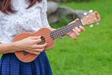 Genç kadın oyun bahçesinde kahverengi ukulele gitar.