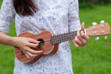 Genç kadın oyun bahçesinde kahverengi ukulele gitar.