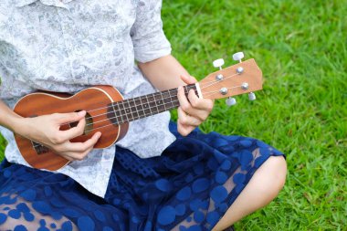 Genç kadın kahverengi Ukulele bahçede oynarken