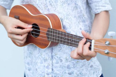 Genç kadın kahverengi Ukulele beyaz veya gri arka planda oynamak.