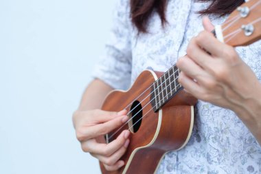 Genç kadın kahverengi Ukulele beyaz veya gri arka planda oynamak.