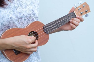 Genç kadın kahverengi Ukulele beyaz veya gri arka planda oynamak.