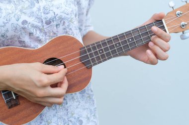 Genç kadın kahverengi Ukulele beyaz veya gri arka planda oynamak.