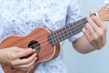 Genç kadın kahverengi Ukulele beyaz veya gri arka planda oynamak.