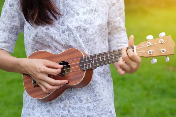 Genç kadın oyun bahçesinde kahverengi ukulele gitar.