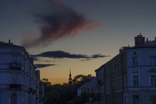 Şehir binaları dramatik alacakaranlık bulutlarının altında uzak bir kilise kulesi silueti oluşturur..