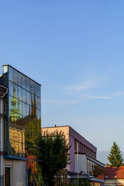 Modern cam cephe tarihi mimariyi, güneşli şehir caddesini ve mavi gökyüzünü yansıtıyor.