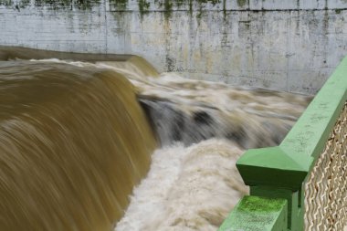 Önünde yeşil güvenlik korkulukları ile baraj yapısının üzerine güçlü bir çağlayan su sızıntısı.