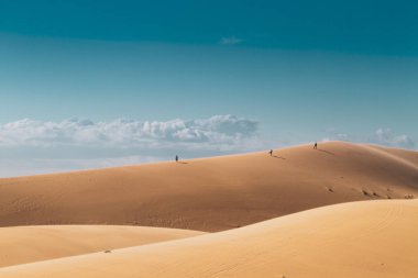 Uzaktaki üç kişi çöldeki bir tepenin üzerinde yürüyor..