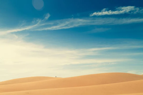 One people in the distance walk on top of a hill in the desert.