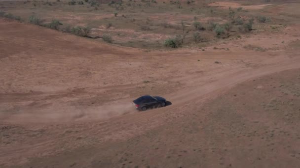 Auto sportiva blu scuro va veloce su strada sabbiosa lasciando nuvole di polvere dietro. — Video Stock