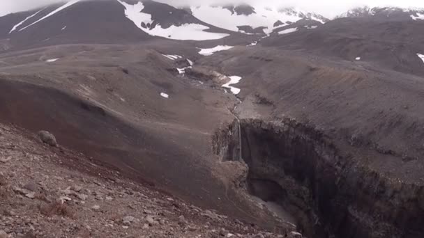 严酷的高山自然 穿过山腰的瀑布 在远处的穆特洛夫斯基火山 灰色的天空 山脉的上升 — 图库视频影像