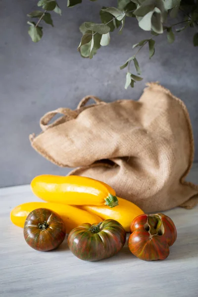灰色の背景とユーカリの葉にカーブトマト 黄色のズッキーニとキャンバスバッグ — ストック写真