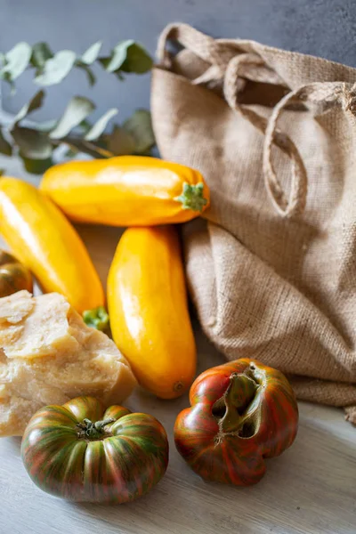 灰色の背景とユーカリの葉にカーブトマト 黄色のズッキーニ パルメザンチーズとキャンバスバッグ — ストック写真