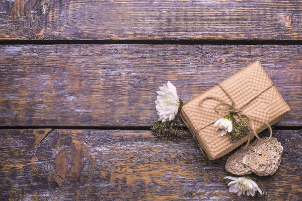 A festive set - a box with a gift, a white flowers, white stone on a wooden old background.