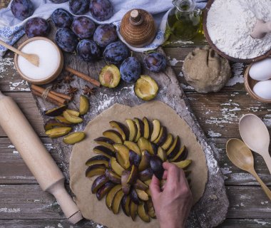 Bir kadın eli Erik için Fransızca ülke pasta üzerinde rulo bir hamur koyar. Taze malzemeler ahşap bir masa üzerinde ev yapımı pasta pişirme için. Üstten görünüm.