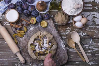 Bir ev yapımı taze doğal lezzetli Fransız ülke pasta grafiğinden Erik ahşap arka plan üzerinde bir el yardımı ile hazırlama süreci.