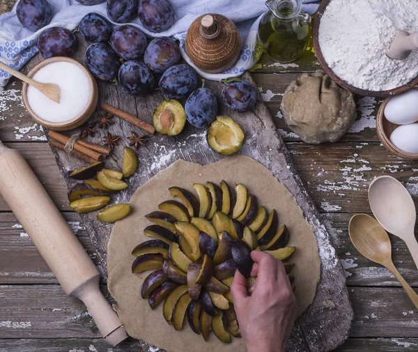 Bir kadın eli Erik için Fransızca ülke pasta üzerinde rulo bir hamur koyar. Taze malzemeler ahşap bir masa üzerinde ev yapımı pasta pişirme için. Üstten görünüm.