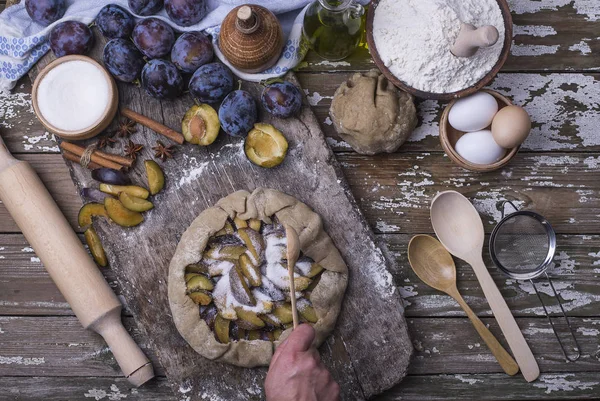 Bir ev yapımı taze doğal lezzetli Fransız ülke pasta grafiğinden Erik ahşap arka plan üzerinde bir el yardımı ile hazırlama süreci.