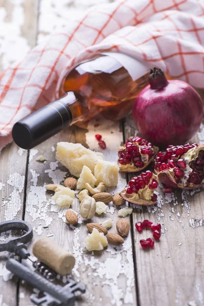 Fresh ripe pomegranate, rose wine in a bottle, almond nuts, cheese on a wooden table with copy space.