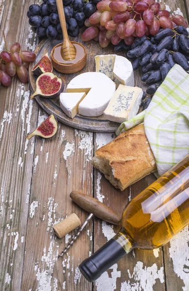 The bottle of white wine with cheese, white bread, fresh grape, pears, figs, honey on a wooden board, background, place for text.