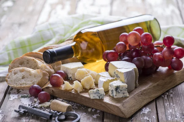 Bottle of white glass and different cheese, bread on a wooden board.