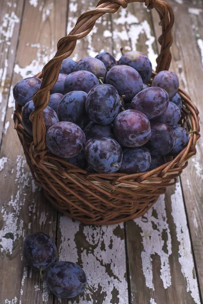 Basket of ripe organic plums on a wooden table. — Stock Photo, Image