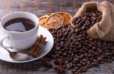 Taze kavrulmuş kahve çekirdekleri ve taze demlenmiş içeceklerle dolu beyaz seramik bardak..