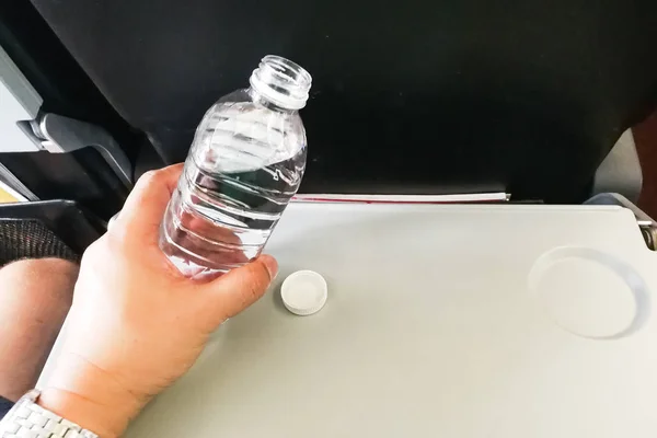 Passenger holding mineral water bottle in aeroplane cabin.  Advice to drink lots of water to keep  oneself hydrated on long haul flight.