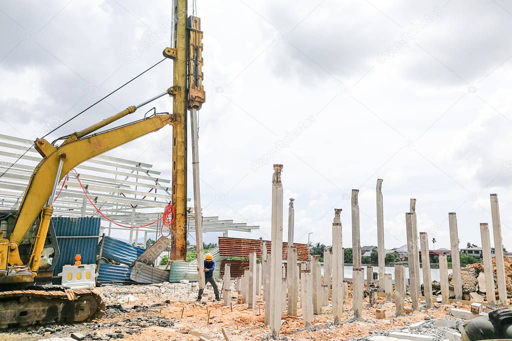 Worker carrying out ground piling work at construction site with heavy machinery