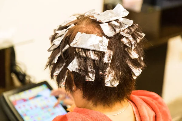 Person\'s hair wrapped with aluminum foil  during chemical color hair dye at salon