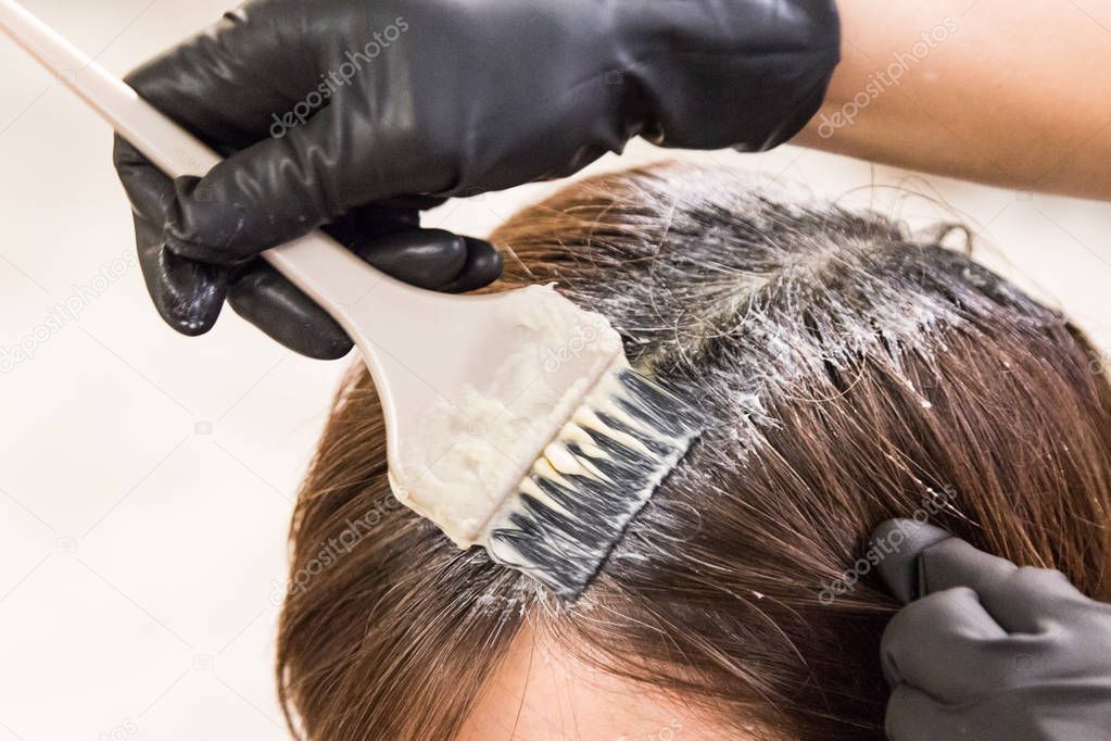 Closeup of hair dresser applying chemical color dye onto hair of customer in salon