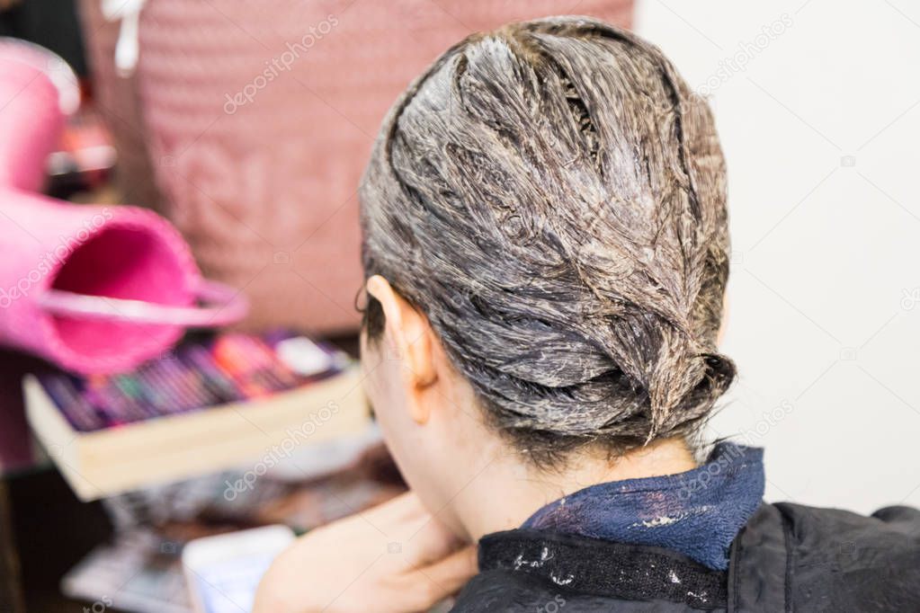 Closeup of hair dresser applying chemical color dye onto hair of customer in salon