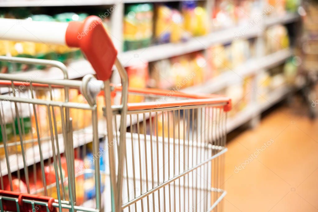 Shopping trolley cart with shallow DOF against modern supermarket aisle blurred background