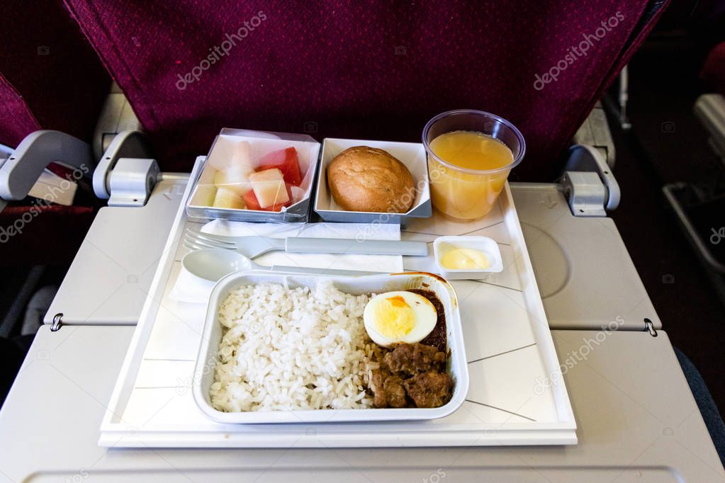Basic inflight meal of economy class consisting rice, egg, beef curry, bread, fruits, and juice.