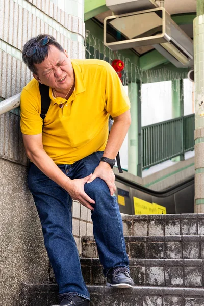 Middle aged man with painful knee struggle walking down flight of stairs in city