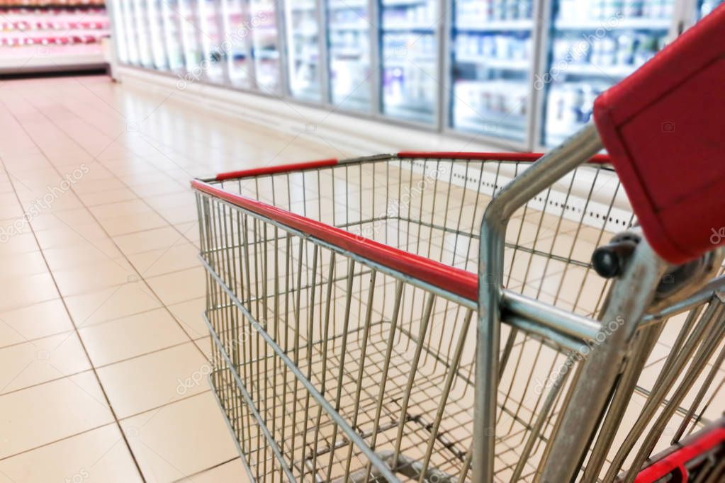 Shopping trolley cart with modern supermarket chiller frozen aisle blurred background
