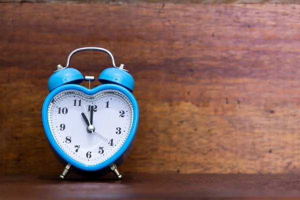 Heart shaped alarm clock on wooden background. Eleven O Clock