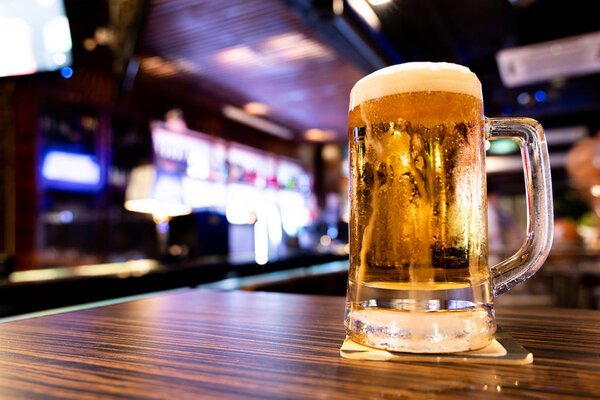 Mug of refreshing draft beer on table with pub background