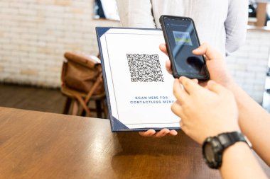 Kişi, yeni normal olarak akıllı telefonlu menü QR kodunu tarıyor. (Fotoğraftaki Sahte Kod)