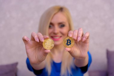 mavi elbiseli güzel bir sarışın kızın elinde iki altın bitcoins