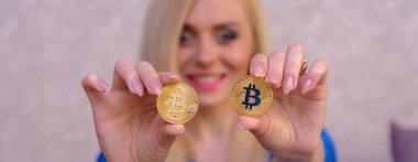 mavi elbiseli güzel bir sarışın kızın elinde iki altın bitcoins