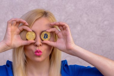 mavi elbiseli güzel bir sarışın kızın elinde iki altın bitcoins