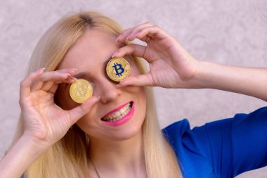 mavi elbiseli güzel bir sarışın kızın elinde iki altın bitcoins