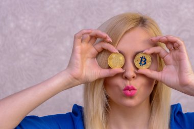 mavi elbiseli güzel bir sarışın kızın elinde iki altın bitcoins