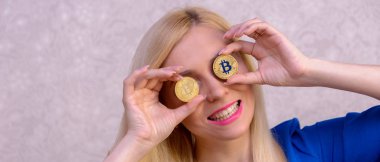 mavi elbiseli güzel bir sarışın kızın elinde iki altın bitcoins