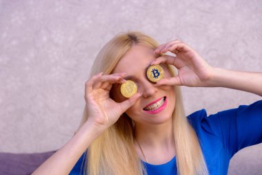 mavi elbiseli güzel bir sarışın kızın elinde iki altın bitcoins