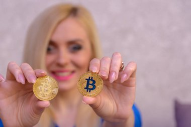 mavi elbiseli güzel bir sarışın kızın elinde iki altın bitcoins