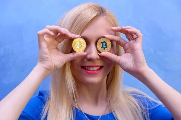 mavi elbiseli güzel bir sarışın kızın elinde altın bitcoin