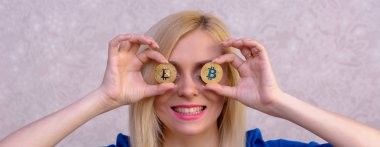 mavi elbiseli güzel bir sarışın kızın elinde iki altın bitcoins